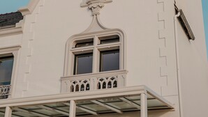 Ein weißes Gebäude mit einem dreieckigen Dach, einem kleinen Fenster und einem Balkon mit Glastrennwand.