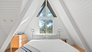 A bedroom with a sloped ceiling, a large window, a bed with white bedding, a wooden dresser, and two bedside tables with lamps. - A-Frame + Indoor Sauna & Hot Tub · Lake Arrowhead (Lake Arrowhead)