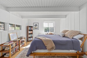 Une chambre à coucher avec un lit en bois, une bibliothèque, un tableau encadré et une fenêtre avec des stores.