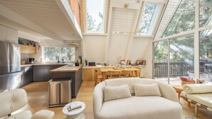 A modern kitchen with a large island, wooden dining table, and a cozy seating area with a sofa and chairs. - A-Frame + Indoor Sauna & Hot Tub · Lake Arrowhead (Lake Arrowhead)