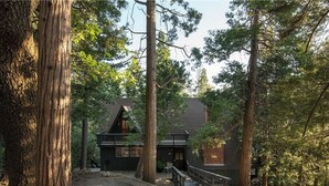 A cabin with a wooden deck, surrounded by tall trees and a clear sky. - A-Frame + Indoor Sauna & Hot Tub · Lake Arrowhead (Lake Arrowhead)