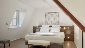 A modern bedroom with a sloped ceiling, a large bed, a bench, and a window.