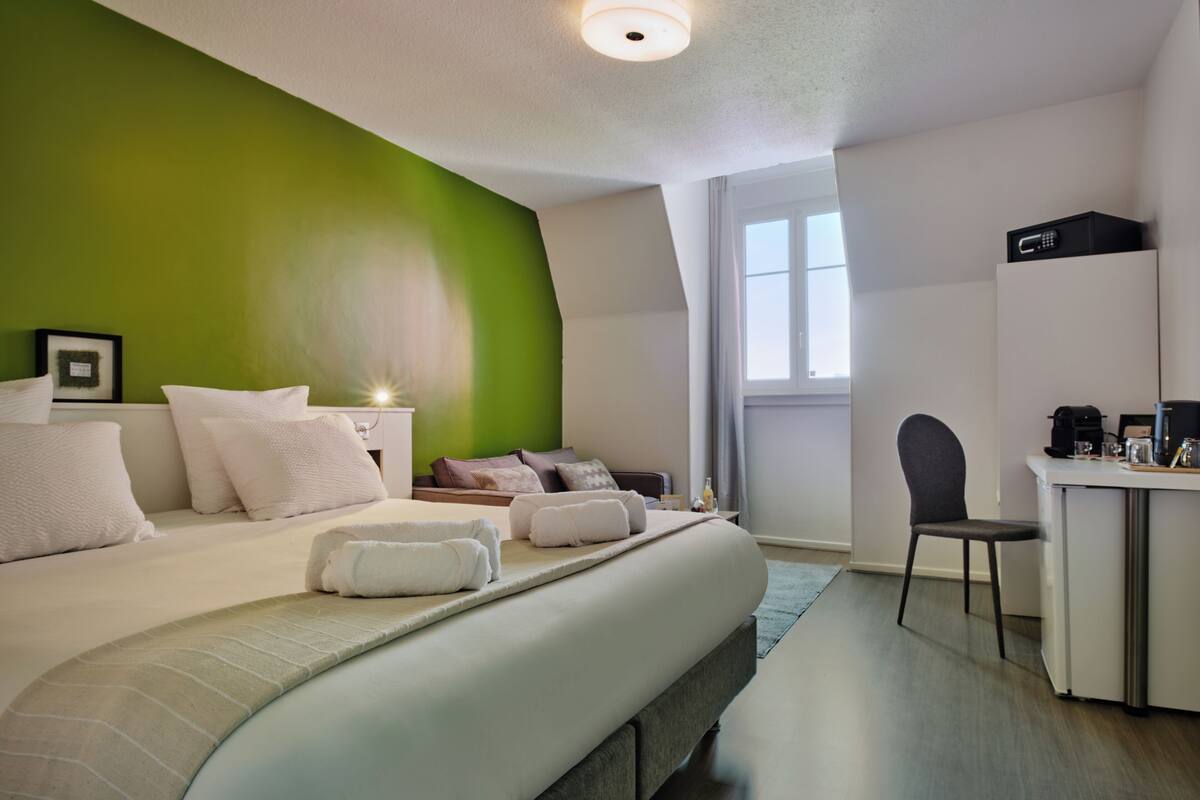 A modern hotel room with a large bed, a desk, and a green accent wall.