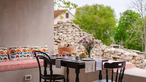 An outdoor dining area with a stone wall, a table set with a vase of flowers, and colorful pillows on a bench. - Amazing home in Gornji Humac Brac (Gornji Humac Brac)