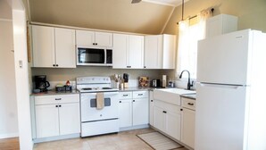 Een moderne keuken met witte kastjes, een roestvrijstalen magnetron, een wit fornuis en een witte koelkast.