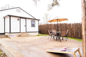 A patio with a table and chairs, a wooden deck, and a white building with black trim. - Charming Getaway in Comfort, TX - Relax, Recharge, Explore - Texas Wine Country (Comfort)