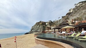 A beach resort with a pool, lounge chairs, and a cliffside view. - Exquisite Escape (Cabo San Lucas)