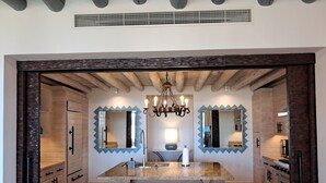 A modern kitchen with a central island, two large mirrors, a chandelier, and wooden cabinetry. - Exquisite Escape (Cabo San Lucas)