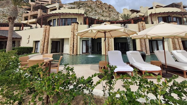 A resort with a swimming pool, lounge chairs, and umbrellas. - Exquisite Escape (Cabo San Lucas)