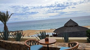 A beachside patio with a table and chairs, a thatched-roof structure, and a view of the ocean. - Exquisite Escape (Cabo San Lucas)