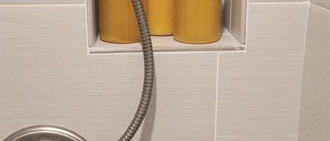 Une salle de bain avec un espace douche comprenant un pommeau de douche à main et trois flacons de savon pour le corps.