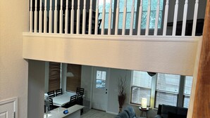 Ein geräumiger Wohnbereich mit hoher Decke, ein Essbereich mit einer Küche im Hintergrund und eine Treppe mit hölzernem Geländer.