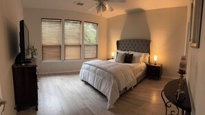 Ein Schlafzimmer mit einem großen Bett, zwei Nachttischen, einem Deckenventilator und einem Fenster mit Jalousien.