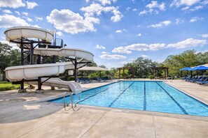 Uma piscina com escorrega, cadeiras de sol e um pérgola.
