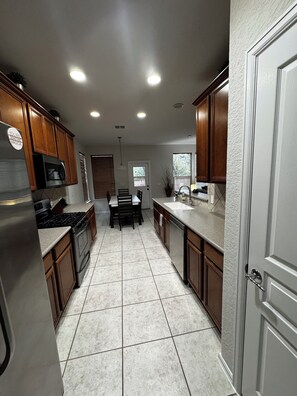 A kitchen with wooden cabinets, a stainless steel refrigerator, a microwave, and a tiled floor.