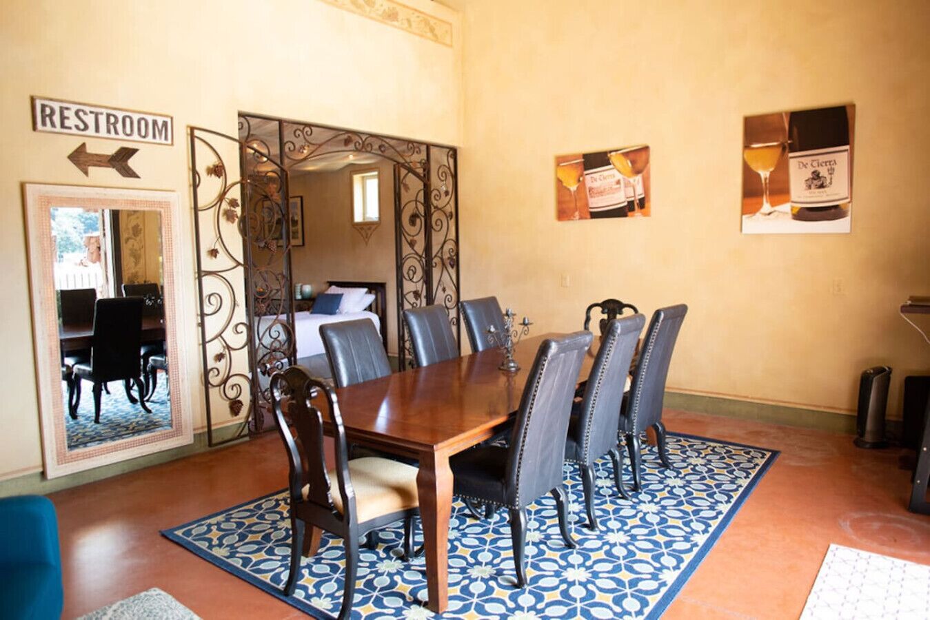 A dining area with a wooden table and six chairs, a blue patterned rug, and a sign indicating a restroom.