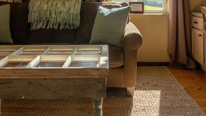 A cozy living room with a large window, a wooden coffee table, a sofa, and framed pictures on the wall. - The Vineyard House in the Pastures of Heaven (Corral de Tierra)