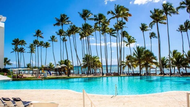 A pool area with palm trees and a view of the ocean.