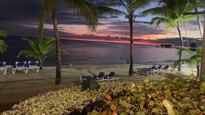 A beach with palm trees, lounge chairs, and a sunset view.