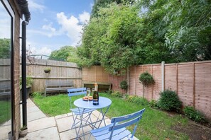 A backyard patio with a round table and blue chairs, a bottle of wine, and a bowl of snacks.