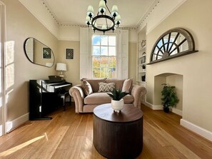 A living room with a piano, a round coffee table, a sofa, and a fireplace.