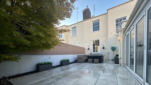 A courtyard with stone flooring, a wooden roofed area, and a glass door leading to a building. - Beautiful 5-Bed Regency Home in Montpellier (Gloucestershire)