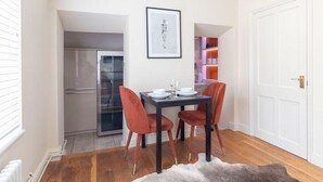 A compact dining area with a table set for two, a refrigerator, and a door leading to a kitchen. - Beautiful 5-Bed Regency Home in Montpellier (Gloucestershire)