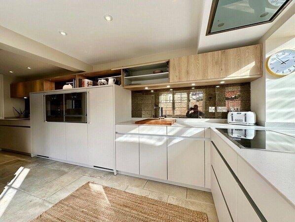 A modern kitchen with white cabinetry, a built-in oven, and a large window providing natural light. - Beautiful 5-Bed Regency Home in Montpellier (Gloucestershire)