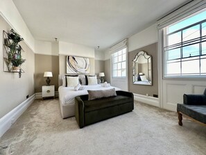 Une chambre à coucher avec un grand lit, un banc sombre, une table de chevet et un miroir.