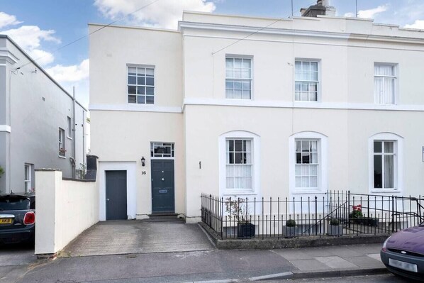 A two-story building with a flat facade, a front door, and a small front yard with a fence and potted plants. - Beautiful 5-Bed Regency Home in Montpellier (Gloucestershire)