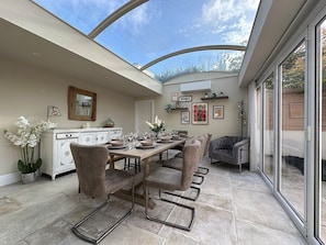 A dining area with a table set for six, surrounded by chairs, a white cabinet, and a mirror on the wall. - Beautiful 5-Bed Regency Home in Montpellier (Gloucestershire)