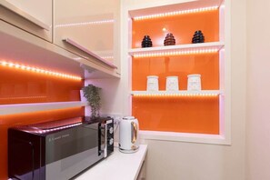 Une cuisine au design moderne, équipée d’un four à micro-ondes encastré, d’une bouilloire et d’étagères pour ranger les ustensiles de cuisine.