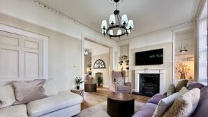 A living room with a fireplace, sofas, and a television. - Beautiful 5-Bed Regency Home in Montpellier (Gloucestershire)