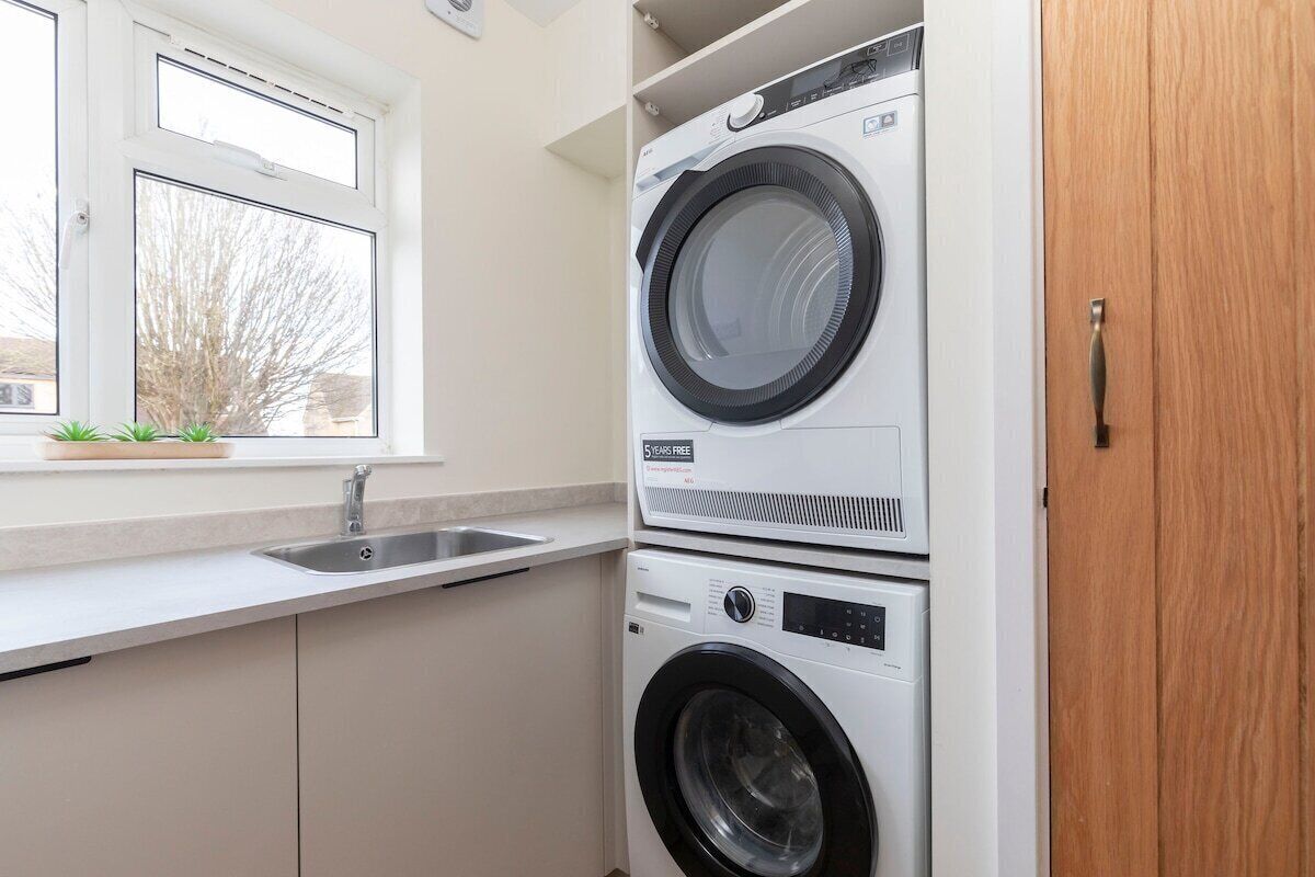 A laundry room with stacked washers and dryers, a window, and a sink.