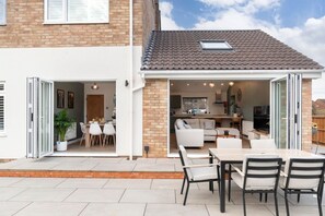 A modern house with a patio area featuring a dining table and chairs, a kitchen, and a living room with a sofa. - Comfortable & Contemporary 5-Bed 3 Bathroom Home (Gloucestershire)