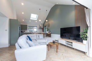 Een moderne woonkamer met een modulaire bank, een flatscreen televisie en een eethoek op de achtergrond.