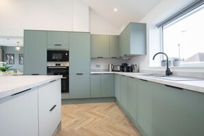 Una cocina moderna con armarios verde claro, horno empotrado y un amplio ventanal que proporciona luz natural.