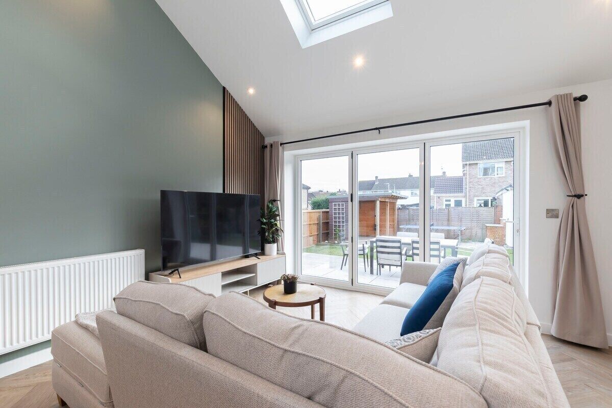 A modern living room with a large flat-screen TV, a beige sofa, a small round table, and a sliding glass door leading to a patio.
