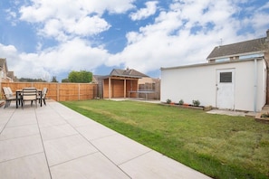 Ein Garten mit Terrasse, Holzfence, Gartenhaus und Rasenfläche.
