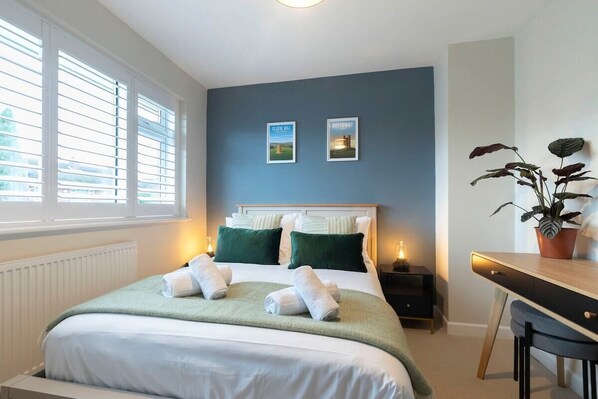 A neatly arranged bedroom with a bed, bedside tables, a desk, and a potted plant.