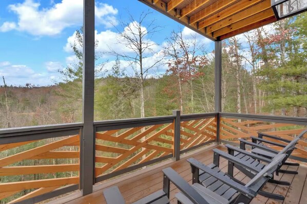 Une terrasse extérieure couverte, dotée de rampes et de bancs en bois, qui offre une vue sur une zone boisée.
