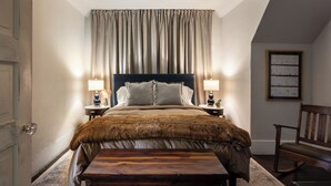 Une chambre à coucher avec un grand lit, deux tables de chevet avec des lampes, un banc, une chaise et un tableau encadré au mur.