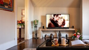 Un salon avec un téléviseur diffusant un film, une table basse sur laquelle sont posées des tasses et une bibliothèque ornée d’objets décoratifs.