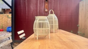 Une table en bois, avec deux lanternes blanches devant une remise rouge.