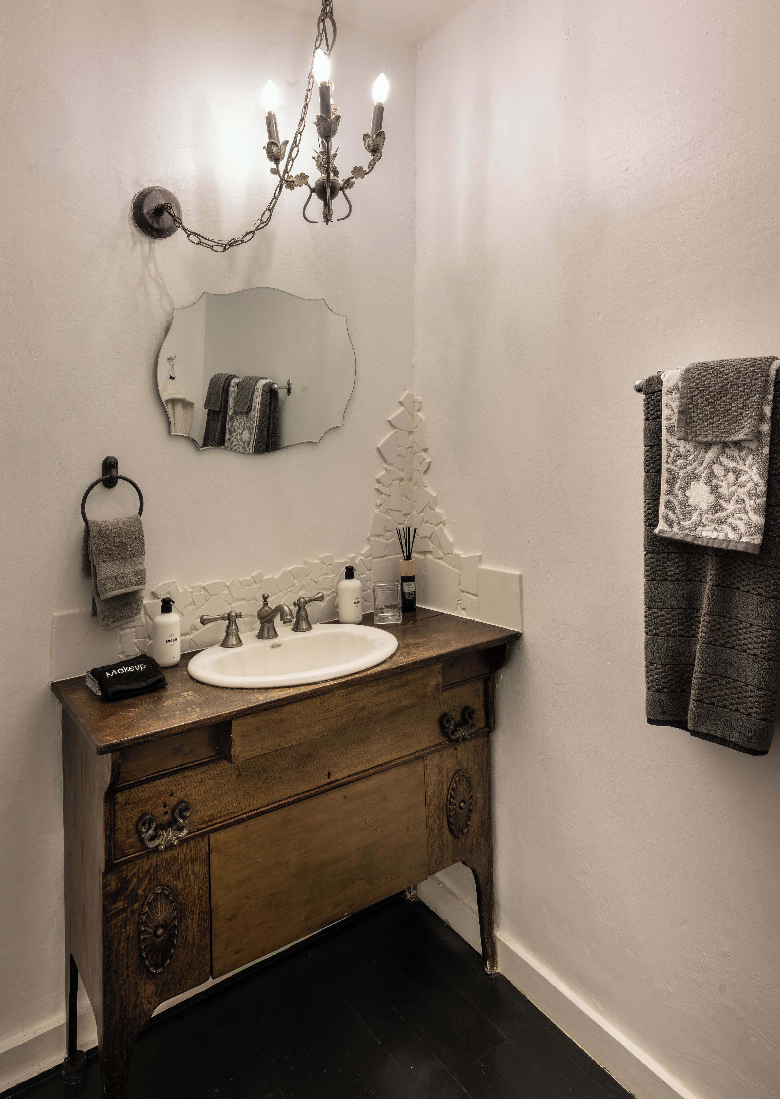 A bathroom with a wooden vanity, a white sink, a mirror, a chandelier, and a towel rack.