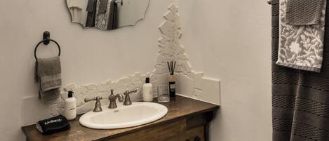 A bathroom with a wooden vanity, a white sink, a mirror, a chandelier, and a towel rack.