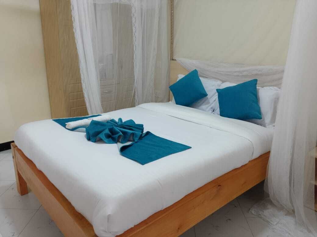 A neatly made bed with white and blue bedding, a wooden frame, and a blue towel on the bed.
