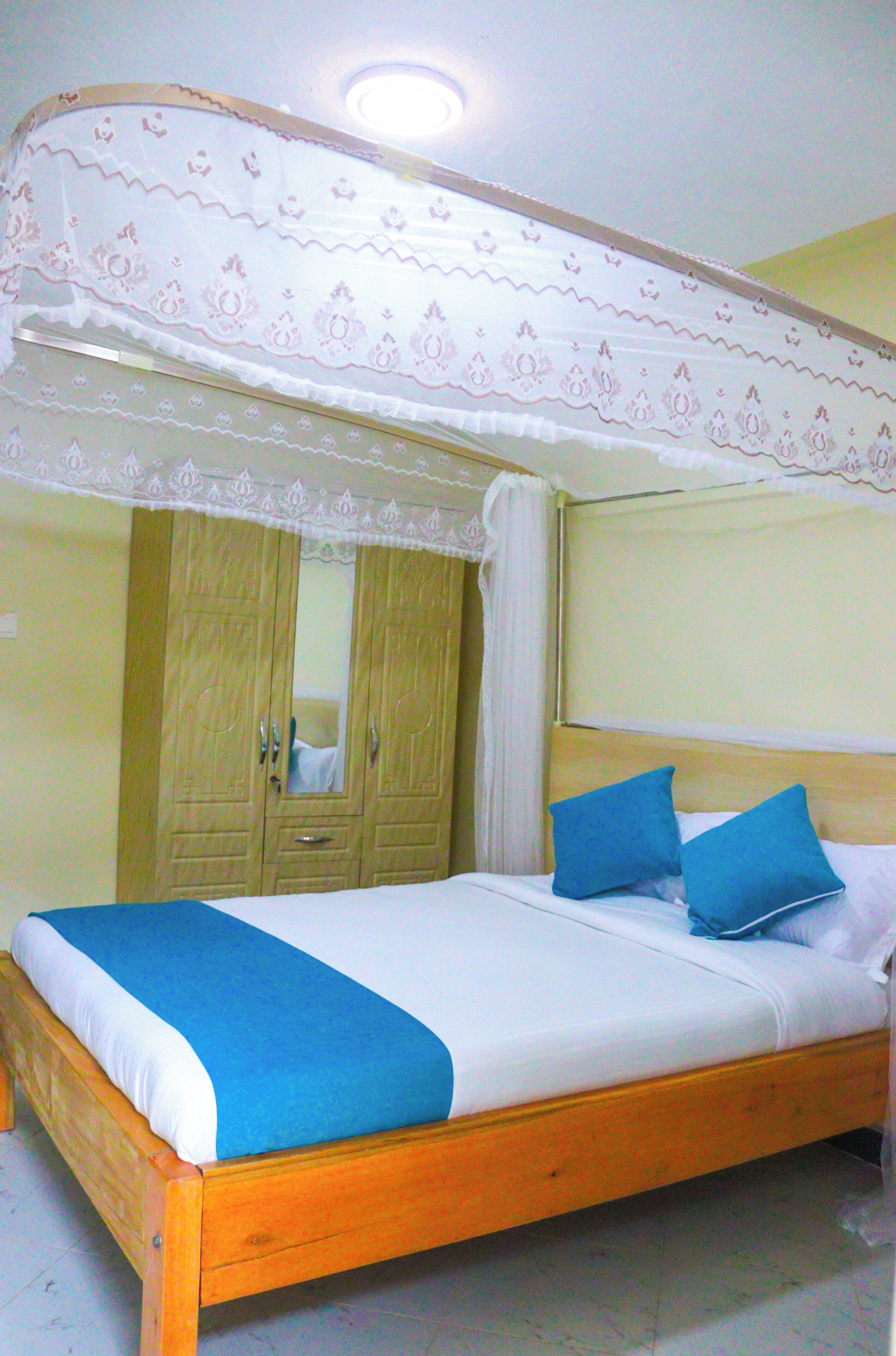 Une chambre avec un lit simple, un lit à baldaquin, une armoire en bois et un miroir.