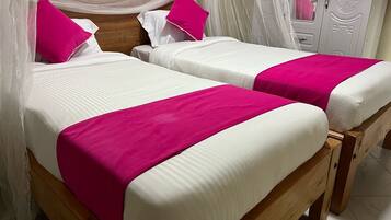 A double bed with white and pink bedding, a wooden headboard, and a canopy.