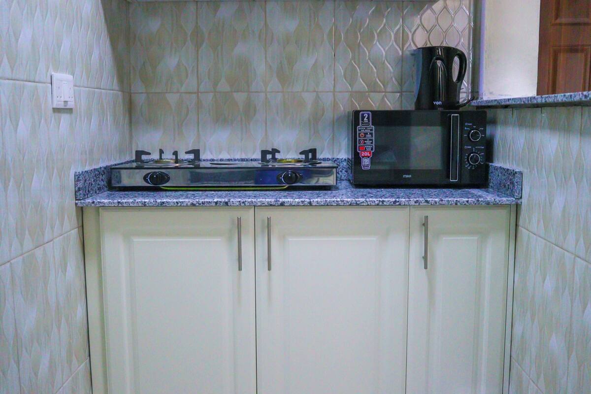 A kitchen with a gas stove, a microwave, and a kettle on the countertop.